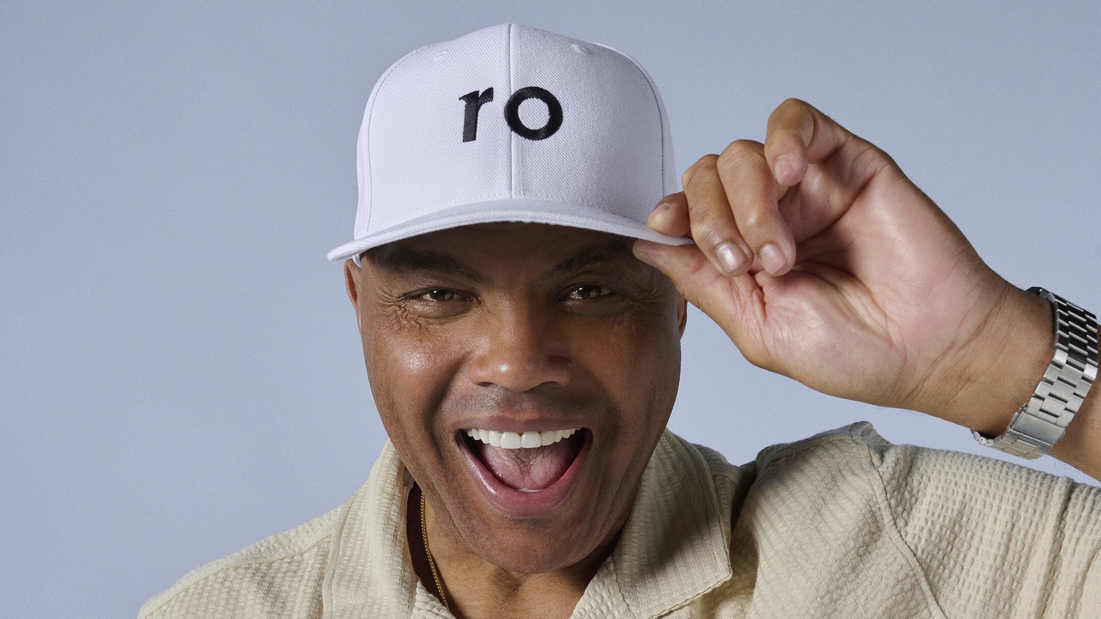 A close up of a smiling Charles Barkley wearing a white Ro baseball cap